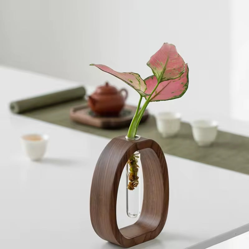 Mini-Glasvase mit walnussfarbenem Holzhalter und rosa Blättern auf einem Tisch